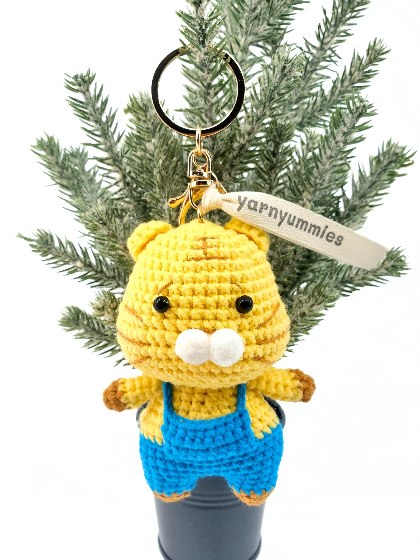 A small, handmade amigurumi keychain depicting a yellow and blue cat, made from cotton yarn, displayed on a key.