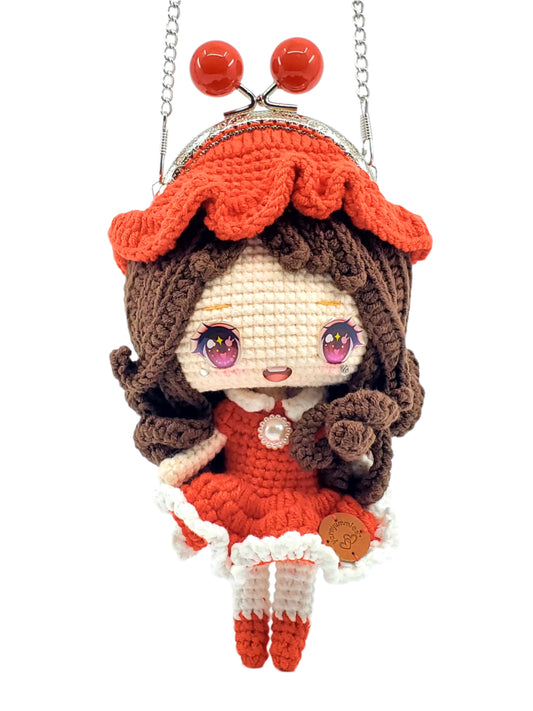 A handmade cotton yarn Brunette Lady Doll Mini Purse with a metal chain strap, dressed in a red dress with white trim and a pearl-like button, featuring flowing brunette curls.