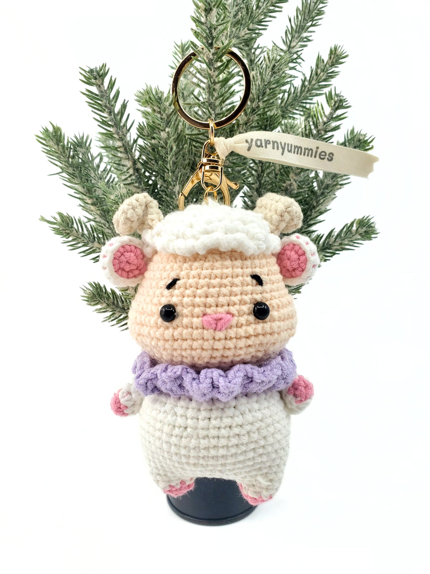 A handmade amigurumi sheep keychain, crafted from white and purple yarn, with a tag reading 'yarnymphs'.