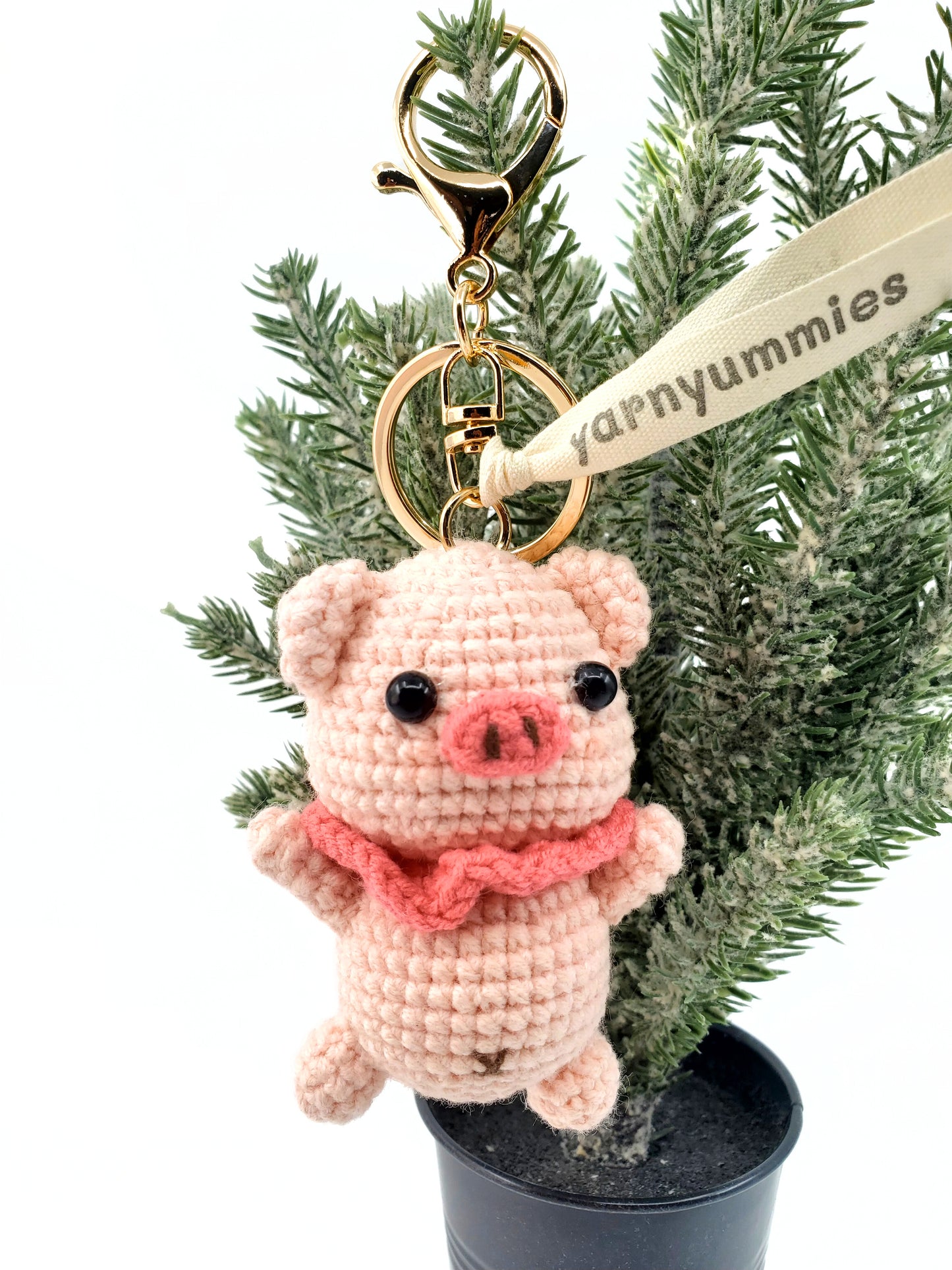 A handmade cotton yarn piggy keychain in beige, pink, and purple colors, displayed on a keychain attachment with a car key fob in the background.