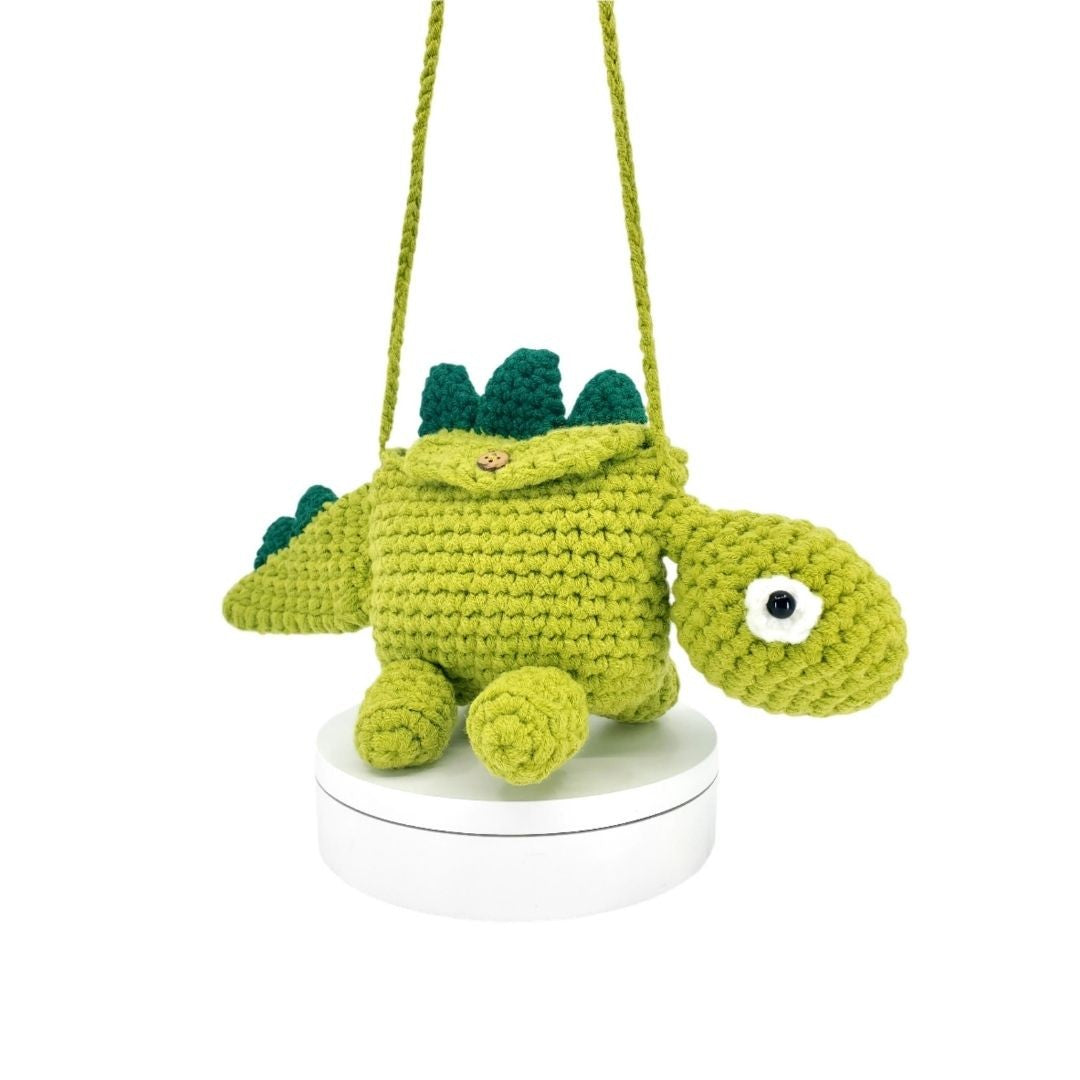 Crocheted dinosaur bag hanging from a string on a white background