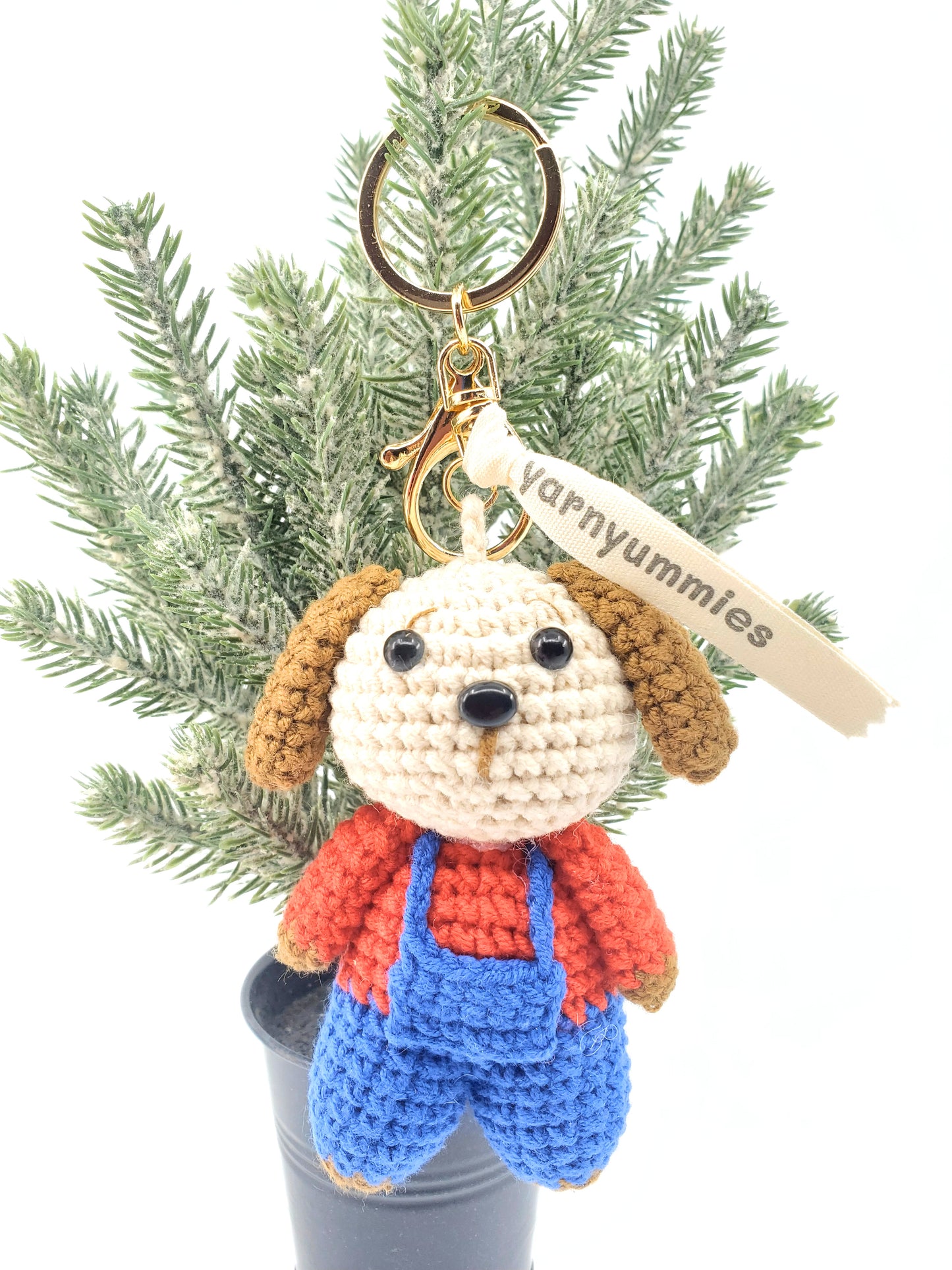 Handmade crochet keychain in the shape of a puppy with a red and blue outfit, next to a car key fob for size comparison.