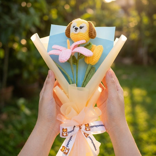 Bouquet of yarn flowers with a small dog-shaped toy held by hands against a blurred green outdoor background.