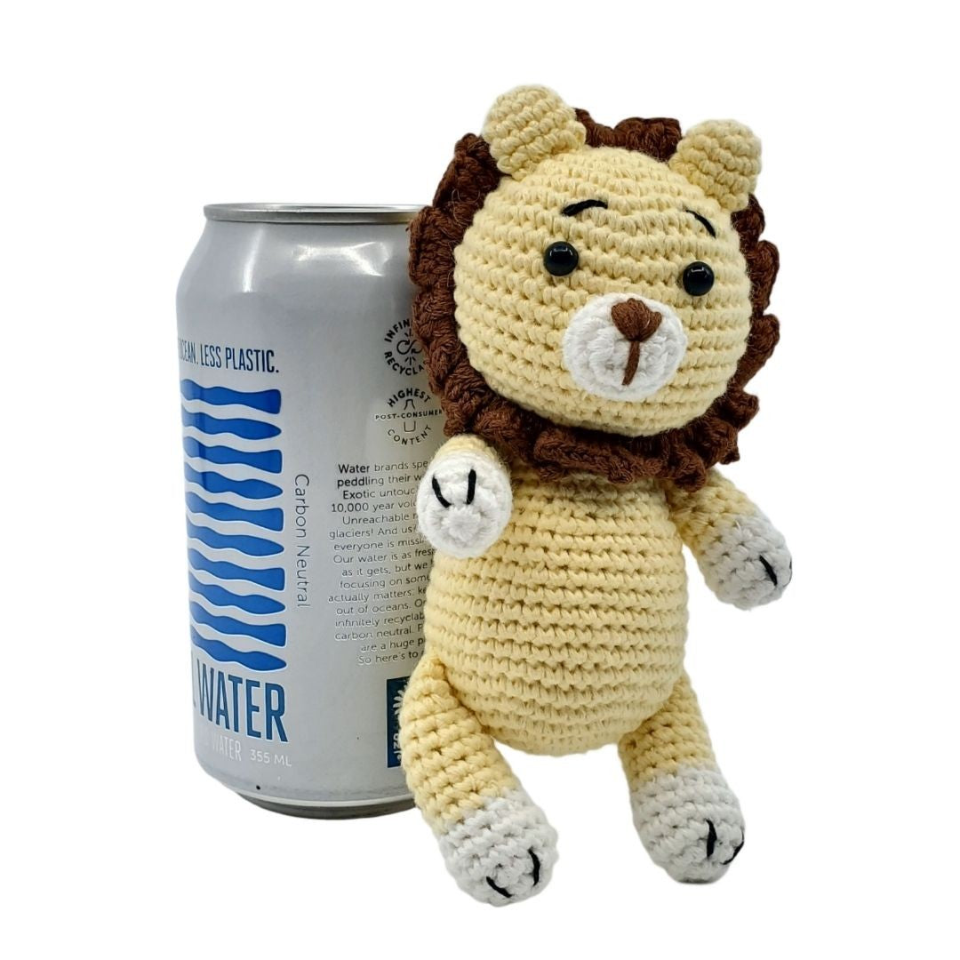 Crocheted lion toy next to a can of water on a white background