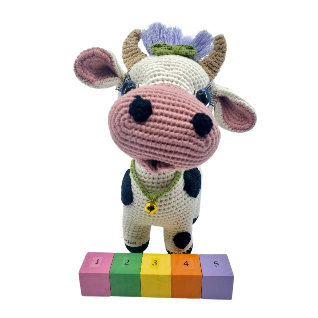Crocheted cow plushie with colorful blocks on a white background