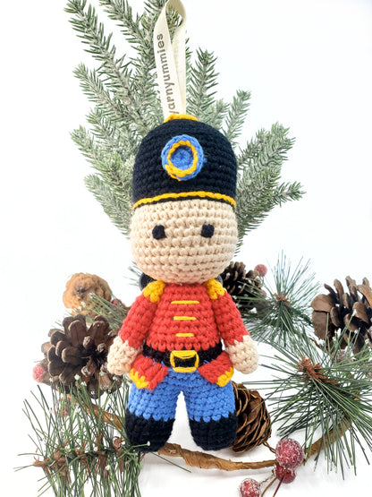Handmade amigurumi-style cotton nutcracker with stitched eyes, wearing a festive hat and outfit, hanging as a Christmas decoration.