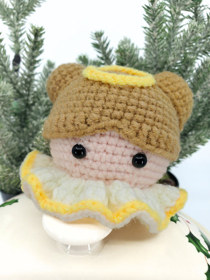 A whimsical Christmas decoration featuring a cute angel made of soft yarn with plastic eyes, set against a holiday-themed backdrop.