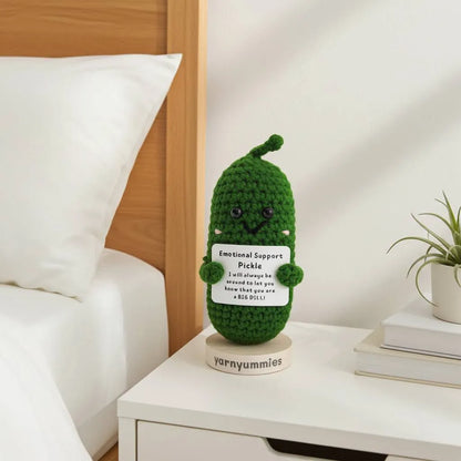 Green crocheted pickle character plush  labeled 'Emotional Support Pickle' on a nightstand.