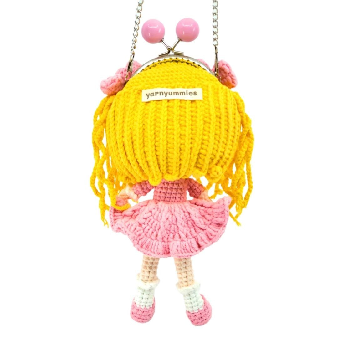 Crocheted doll with yellow hair and pink dress on a white background, featuring the brand 'yarnyummies'.