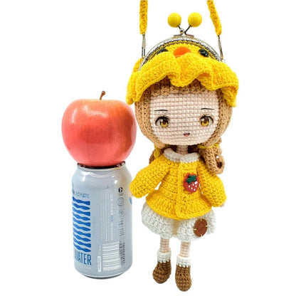 Crocheted doll with yellow outfit and apple on top of a can of water next to it on a white background