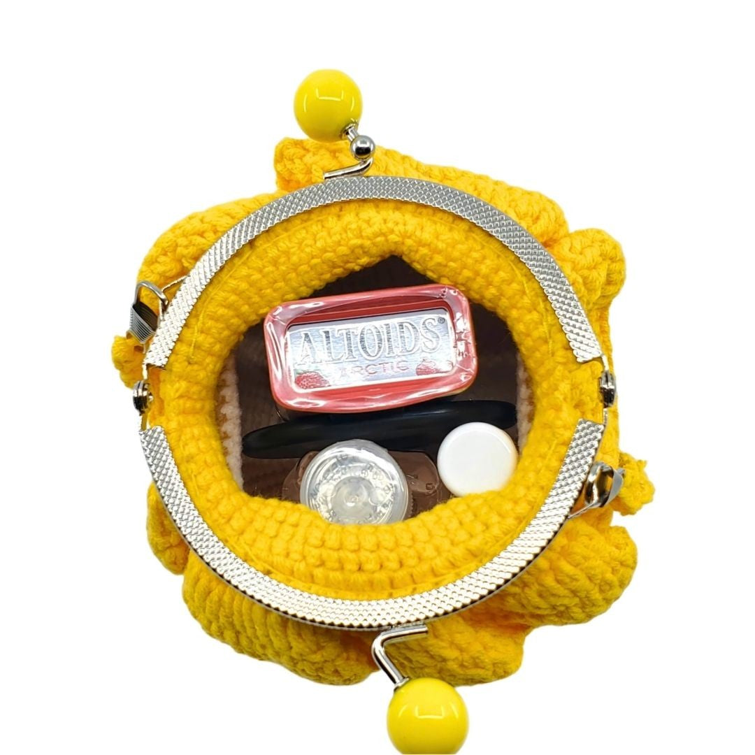 Yellow knitted clutch with a silver frame and a red tin ALTOIDS sign inside on a white background