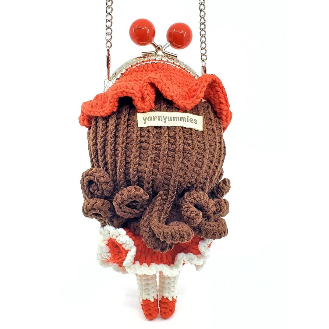 Knitted bag with a brown jead, red top, and red-white skirt on a white background