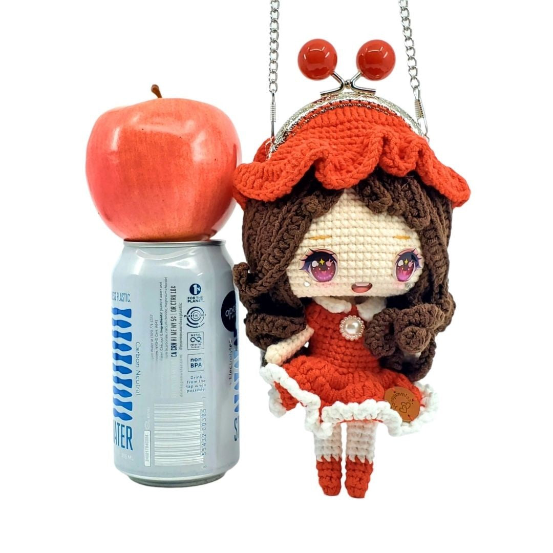 Crocheted doll with red outfit standing next to an apple on top of a can of sparkling can of water.