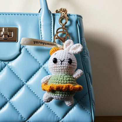 Crocheted bunny keychain with a colorful skirt hanging from a blue handbag.