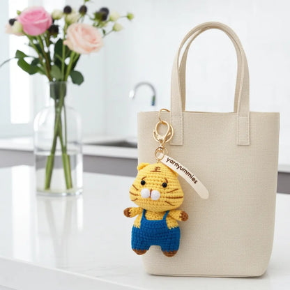 Beige tote bag with a yellow cat-shaped keychain on a white surface.