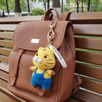 Brown backpack with a yellow plush toy keychain on a wooden bench.