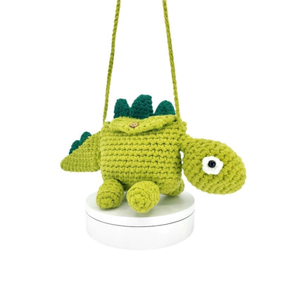 Crocheted dinosaur bag hanging from a string on a white background