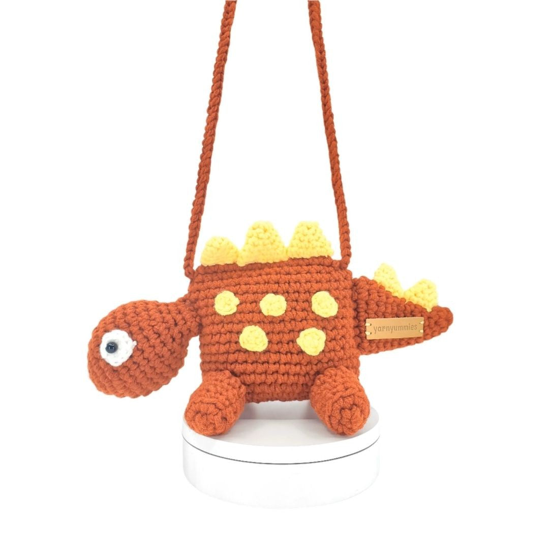 Crocheted dinosaur-shaped bag with a strap on a white background