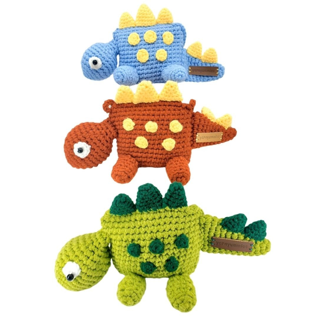 Three colorful crochet dinosaur bags stacked on a white background