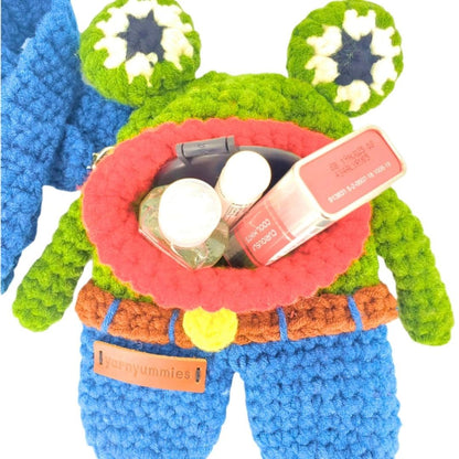 Colorful crocheted frog-shaped bag with lip balm and other items on a white background