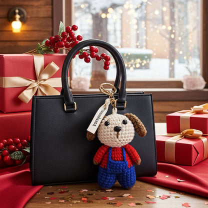 Black handbag with a dog-shaped keychain on a table with Christmas presents and decorations.