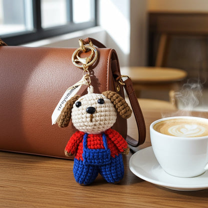 Crocheted dog keychain with a brown leather bag and steaming cup of coffee on a wooden table.