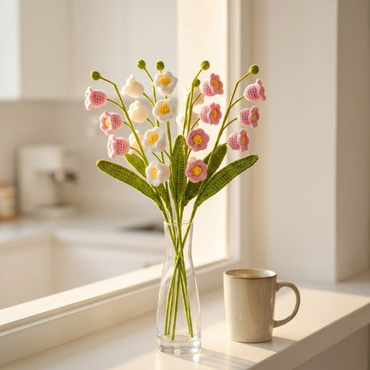 Clear vase with pink and white flowers on a windowsill next to a beige mug.