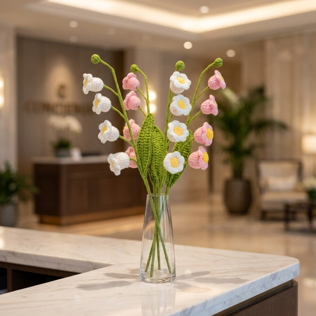 Decorative crocheted flowers in a clear vase on a marble surface with a blurred indoor setting.