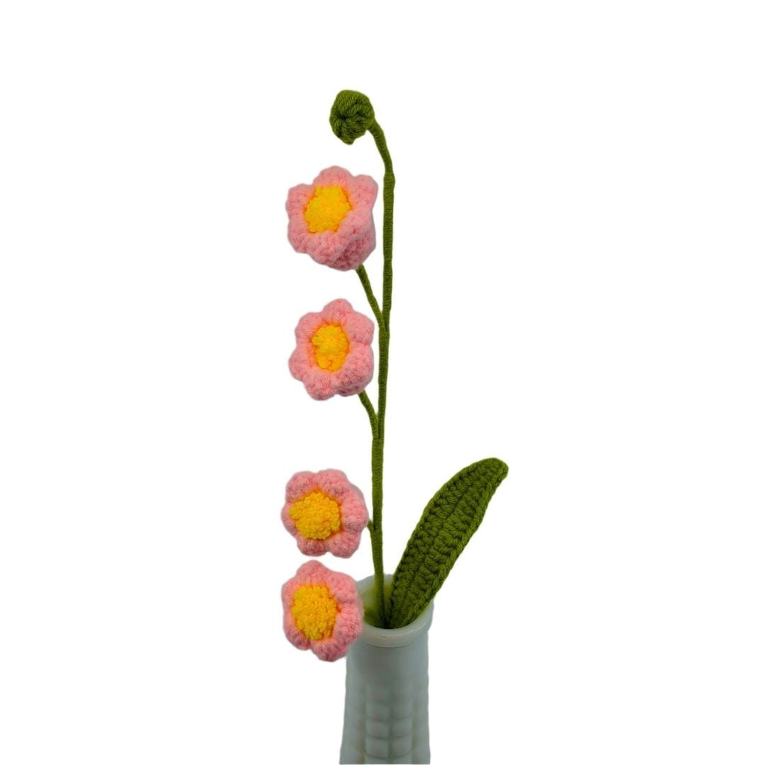 Knitted flowers with pink petals and yellow centers in a white vase on a white background