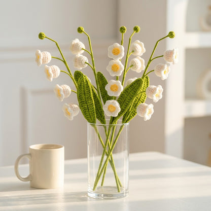 Knitted flower bouquet in a clear vase on a white surface with a blurred background