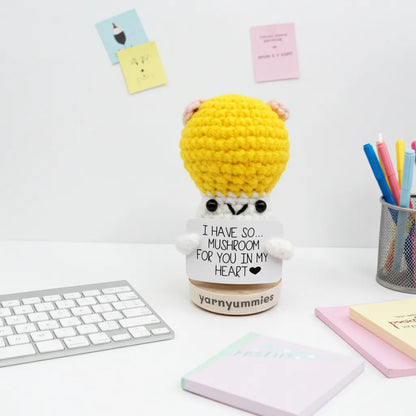 Yellow crocheted mushroom character plush with a white base on a desk with stationery items.