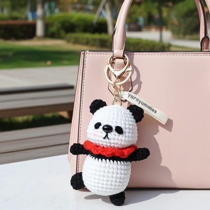 Panda keychain with red scarf attached to a pink handbag outdoors.