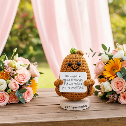 Crocheted pear character with a message card in front of flowers