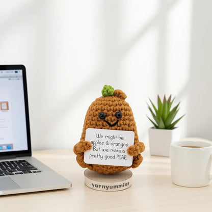 Amigurumi pear-shaped with a humorous message on a desk with a laptop and coffee mug.