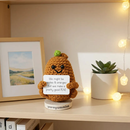 Crocheted pear character holding a sign on a shelf with decor elements