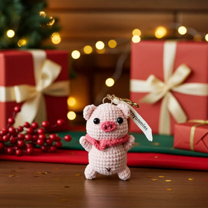 Pink crochet pig keychain with a bow tie in front of Christmas presents and decorations.