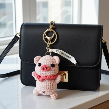 Black handbag with a pink pig-shaped keychain on a light surface.