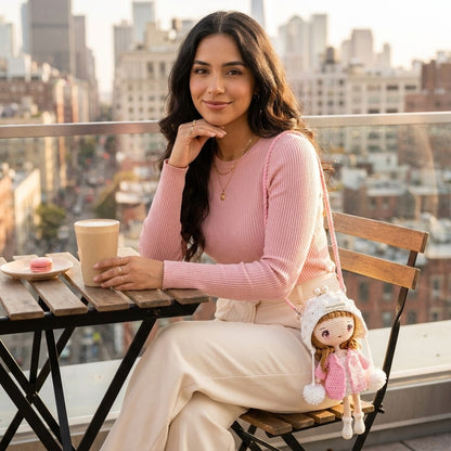 Woman sitting on a rooftop with a cityscape view, holding a coffee cup and carrying a doll bag on shoulder.
