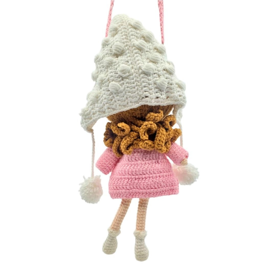 Crocheted doll with a pink dress, brown scarf, and white hat on a white background