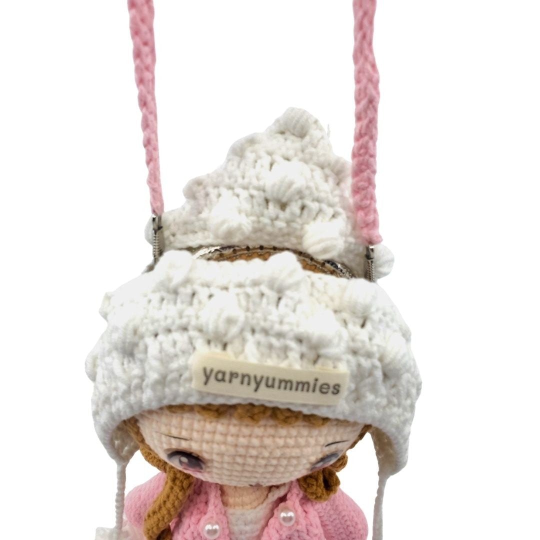 Shoulder bag with a white knitted hat and pink jacket, hanging from a pink string on a white background.