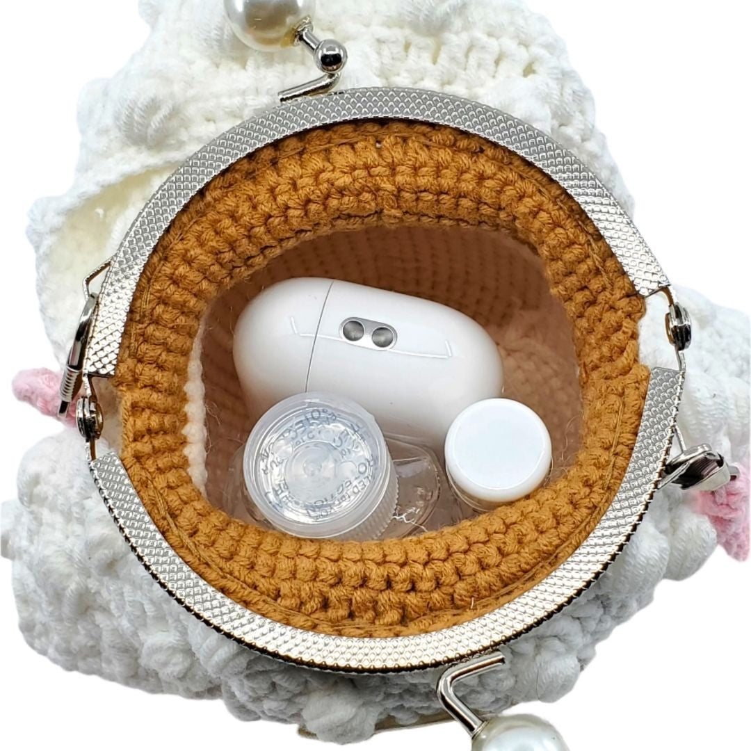 Crocheted pouch with a white electronic device and accessories on a textured white background