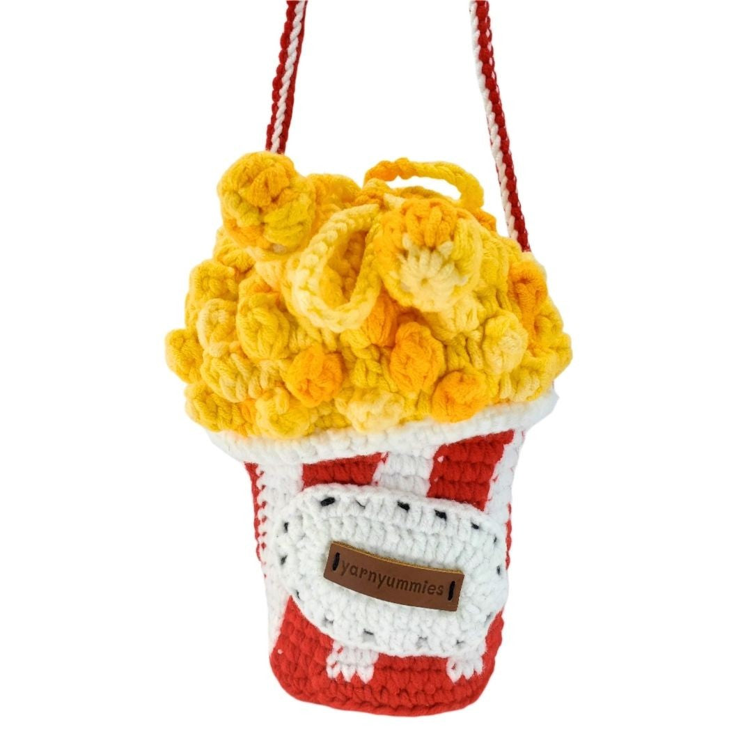 Crocheted popcorn bucket bag and red strap on a white background