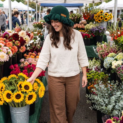 Woman browsing sunflowers at a farmers market wearing a green handmade crochet ruffled brim bucket hat by YarnYummies