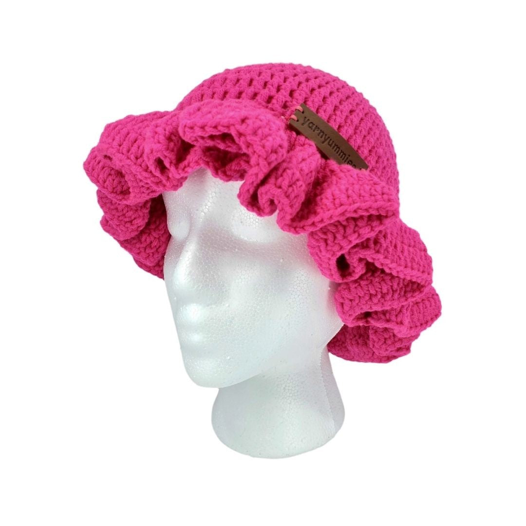 Pink crocheted ruffled brim bucket hat on a mannequin head with a visible brand label against a white background