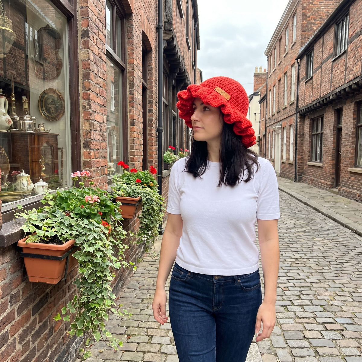 Woman wearing a red handmade crochet ruffled brim bucket hat by YarnYummies on a cobblestone street with brick storefronts