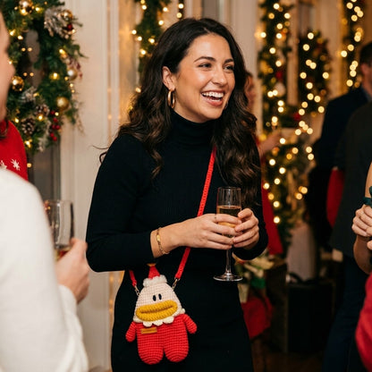 Woman holding a glass of champagne with a festive background and wearing a crocheted santa designed bag