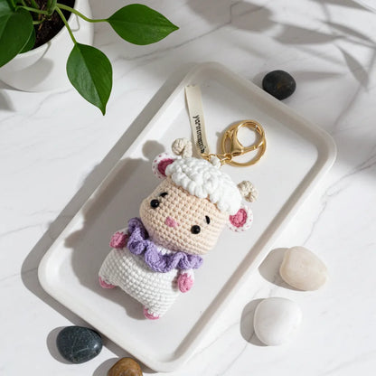 Crocheted keychain with a cute design on a white surface with rocks and a plant.