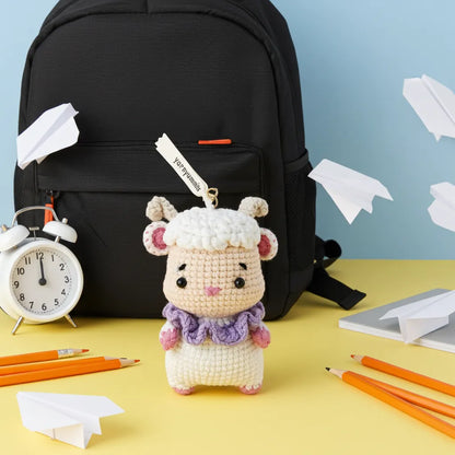 Crocheted sheep keychain with a backpack, alarm clock, and stationery on a yellow surface.