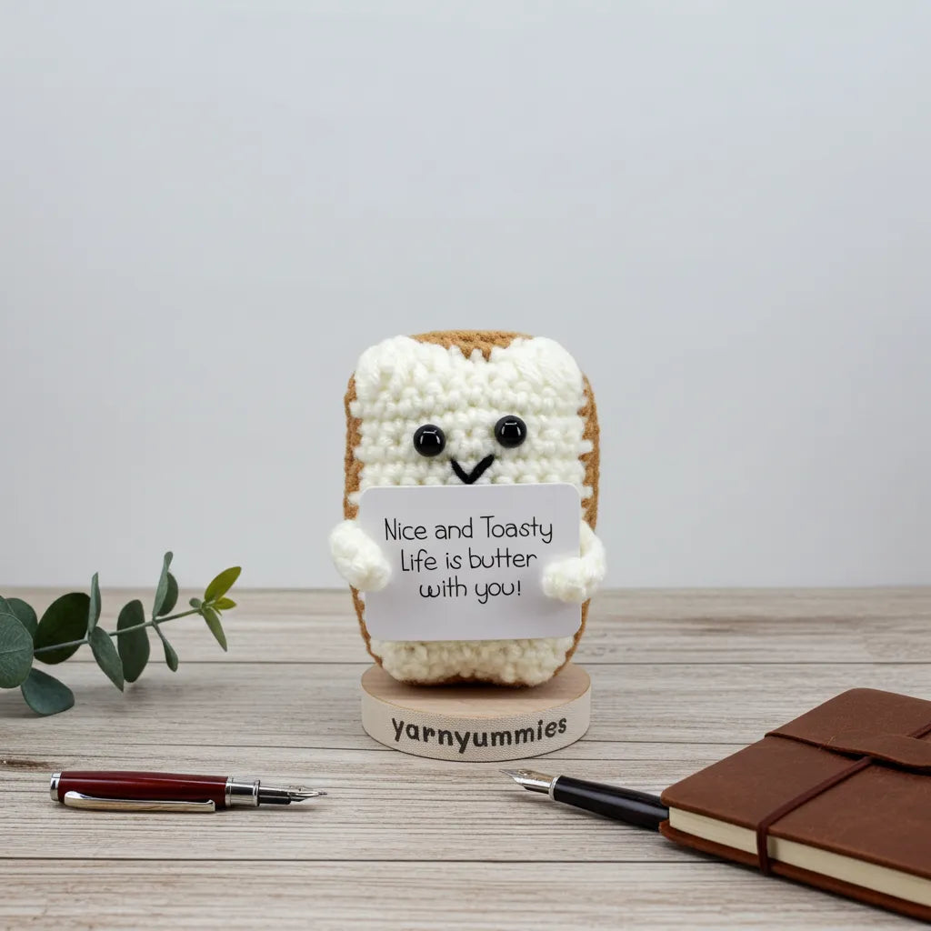 Crocheted toast character with a sign on a wooden stand, surrounded by a pen and notebook.