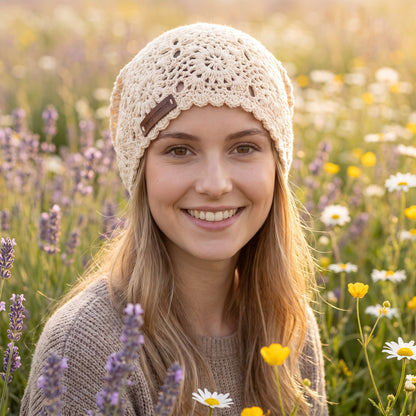 Woman smiling in a wildflower field wearing a cream handmade crochet slouchy beanie by YarnYummies with an open lace stitch pattern
